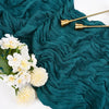 A deep teal fabric draped with crinkled folds, featuring gold-toned metal spoons and white flowers.