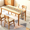 A light wood dining table set with a colorful Day of the Dead Mexican Fiesta table runner on a patterned rug.