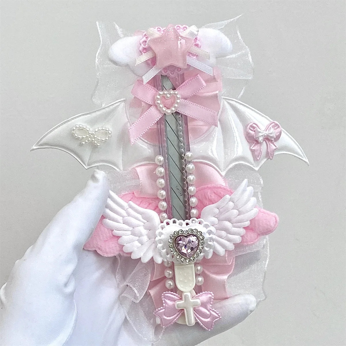 A pink and white decorative utility cutter shaped like a cat paw with a ribbon bow and a cross detail.