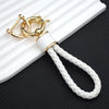 Gold and white braided TPU key fob cover with a leather loop resting on a white surface.