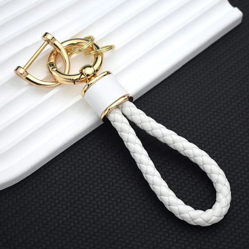 Gold and white braided TPU key fob cover with a leather loop resting on a white surface.