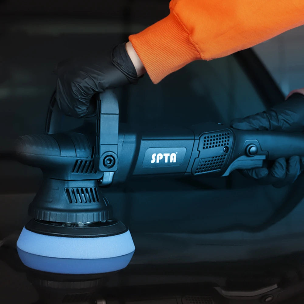A hand wearing an orange sleeve and black glove is operating a black dual action polisher with a 15mm orbit attachment for ca