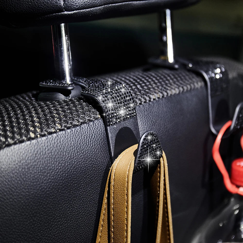 Close-up of a black car seat storage hook set with crystal diamond accents and tan leather strap.