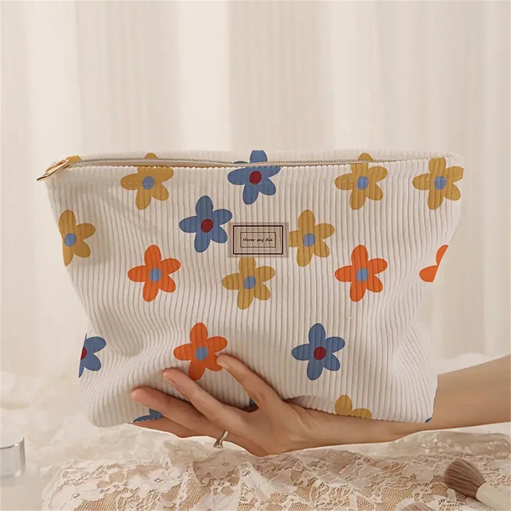 A cream-colored floral corduroy makeup bag with a secure zipper is held in a person's hand.