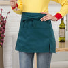 A woman wearing a dark teal half apron with pockets over a yellow top and jeans.