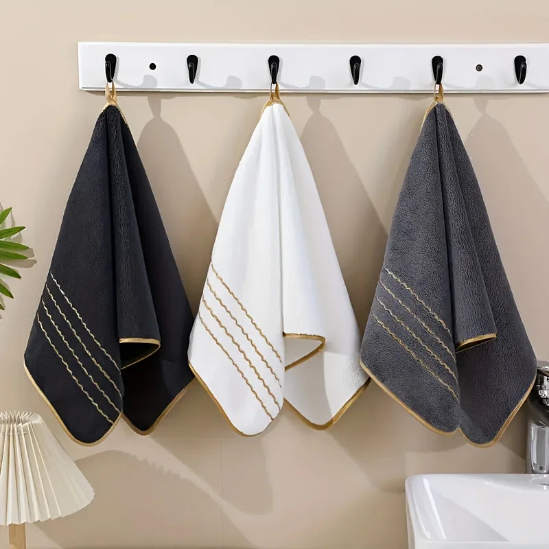 Three gold-striped towels hanging on a white rack against a beige wall.