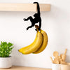 A black monkey silhouette is hanging from a wooden wall hook, with bananas visible below.