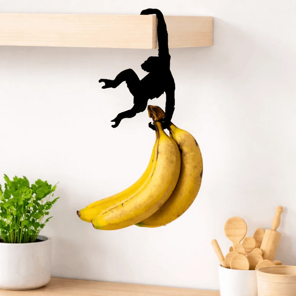 A black monkey silhouette is hanging from a wooden wall hook, with bananas visible below.