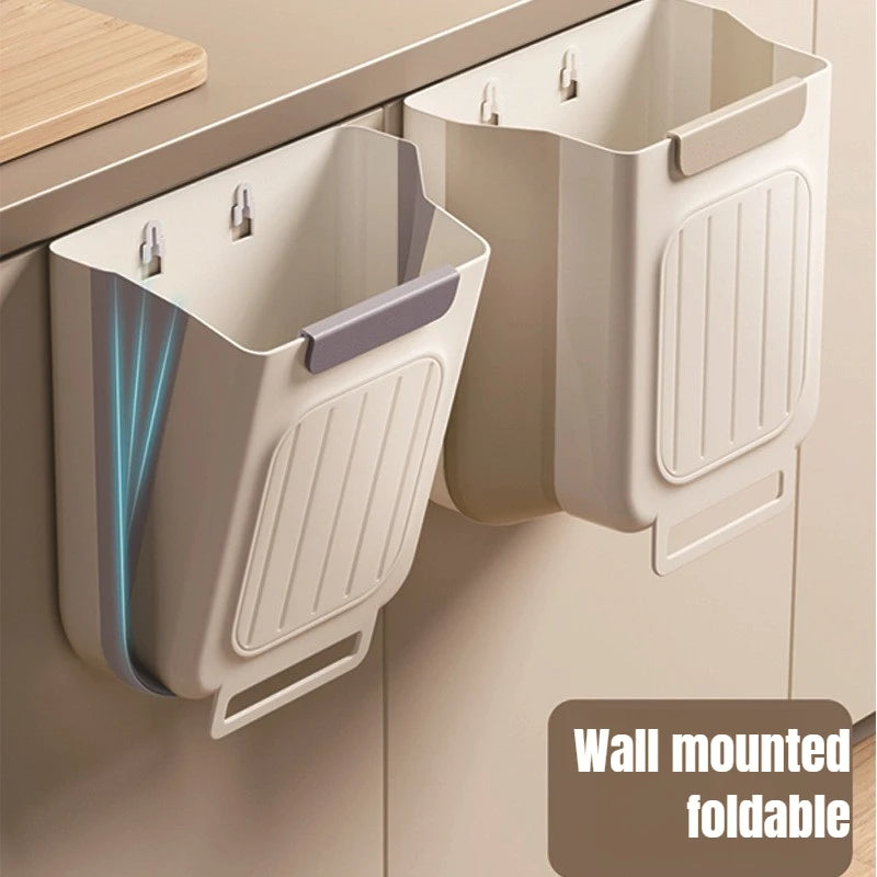 A wall-mounted foldable trash bin with a light beige color is shown hanging on a cabinet.