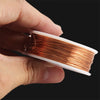 A hand holds a spool of bare copper wire with multiple diameters, showing the shiny reddish-brown metal.