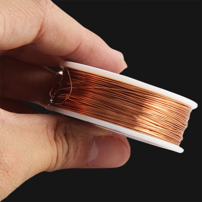 A hand holds a spool of bare copper wire with multiple diameters, showing the shiny reddish-brown metal.