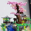 A miniature diorama built with LEGO bricks featuring a pink sakura tree and traditional Japanese-style buildings.