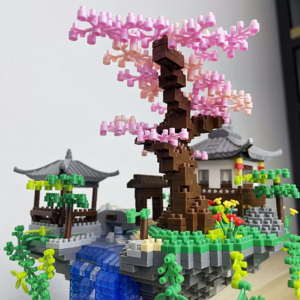 A miniature diorama built with LEGO bricks featuring a pink sakura tree and traditional Japanese-style buildings.
