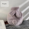 A soft purple plush rabbit hot water bottle with a fluffy flannel cover resting on a gray fabric.