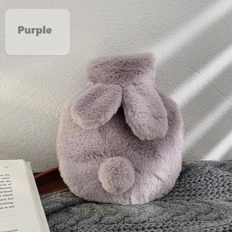 A soft purple plush rabbit hot water bottle with a fluffy flannel cover resting on a gray fabric.