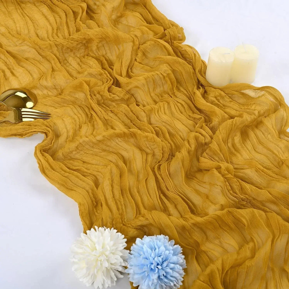 A golden yellow cotton gauze table runner with wavy texture, featuring white candles and blue and white flowers.