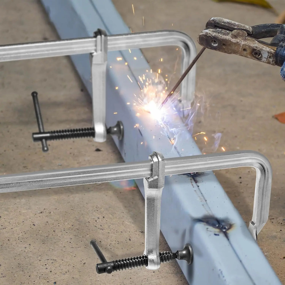 Nahaufnahme eines Satzes aus Forged-Stahl-Klemmen zur Sicherung einer Metallstange mit Funke einer Schweißnaht.