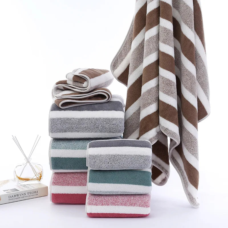 A stack of striped microfiber towels in shades of brown, gray, and pink are displayed next to a small glass object.