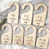 Set of seven wooden baby closet divider hangers marked with age ranges from newborn to 24 months