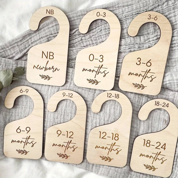 Set of seven wooden baby closet divider hangers marked with age ranges from newborn to 24 months