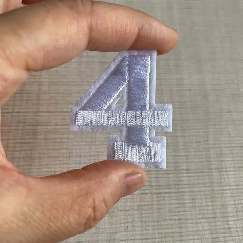A hand holds a light purple iron-on 3D number patch shaped like the numeral four.