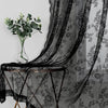 Rideaux en dentelle florale noire drapés sur une table avec un vase de feuillage vert.
