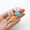 A hand holds several clear and colored acrylic heart beads for jewelry making