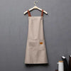 A beige waterproof kitchen apron hanging on a wooden hanger.