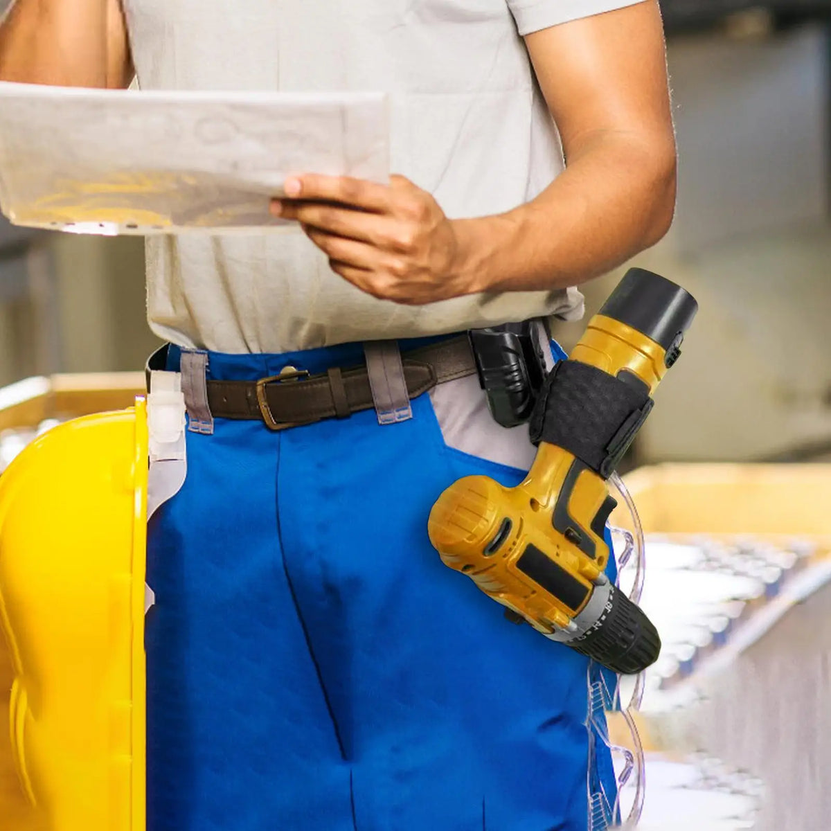 A person wearing blue pants holds a clipboard and a yellow cordless drill attached to a belt clip.