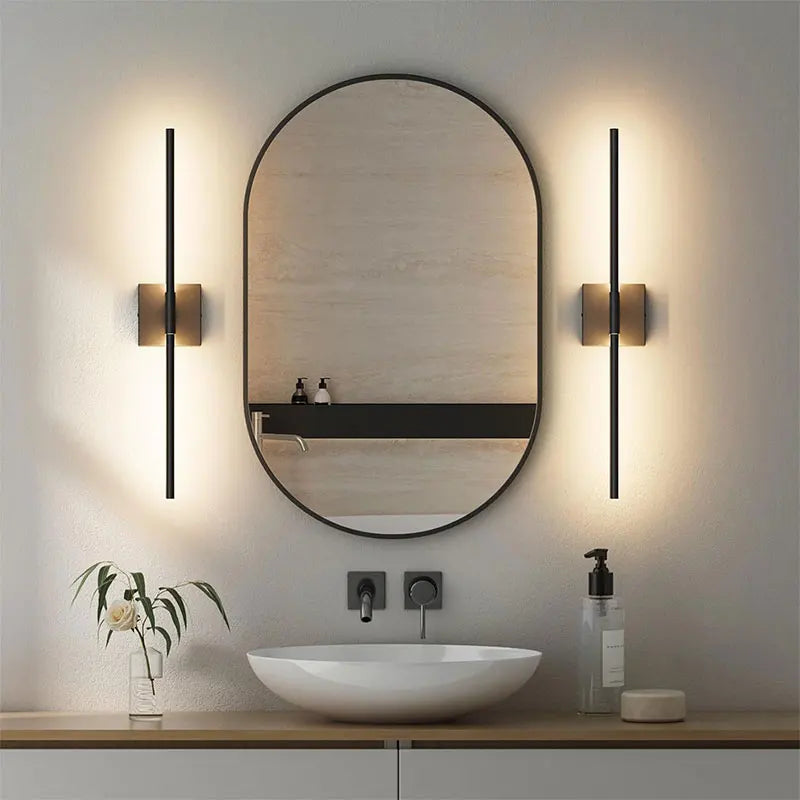 A round mirror above a white vessel sink is illuminated by modern wall sconces.