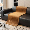 A brown quilted plush sofa cover with a textured weave is draped over a black leather sofa.