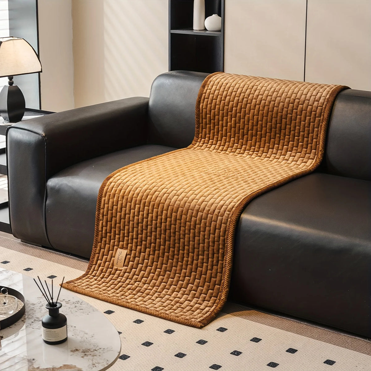 A brown quilted plush sofa cover with a textured weave is draped over a black leather sofa.