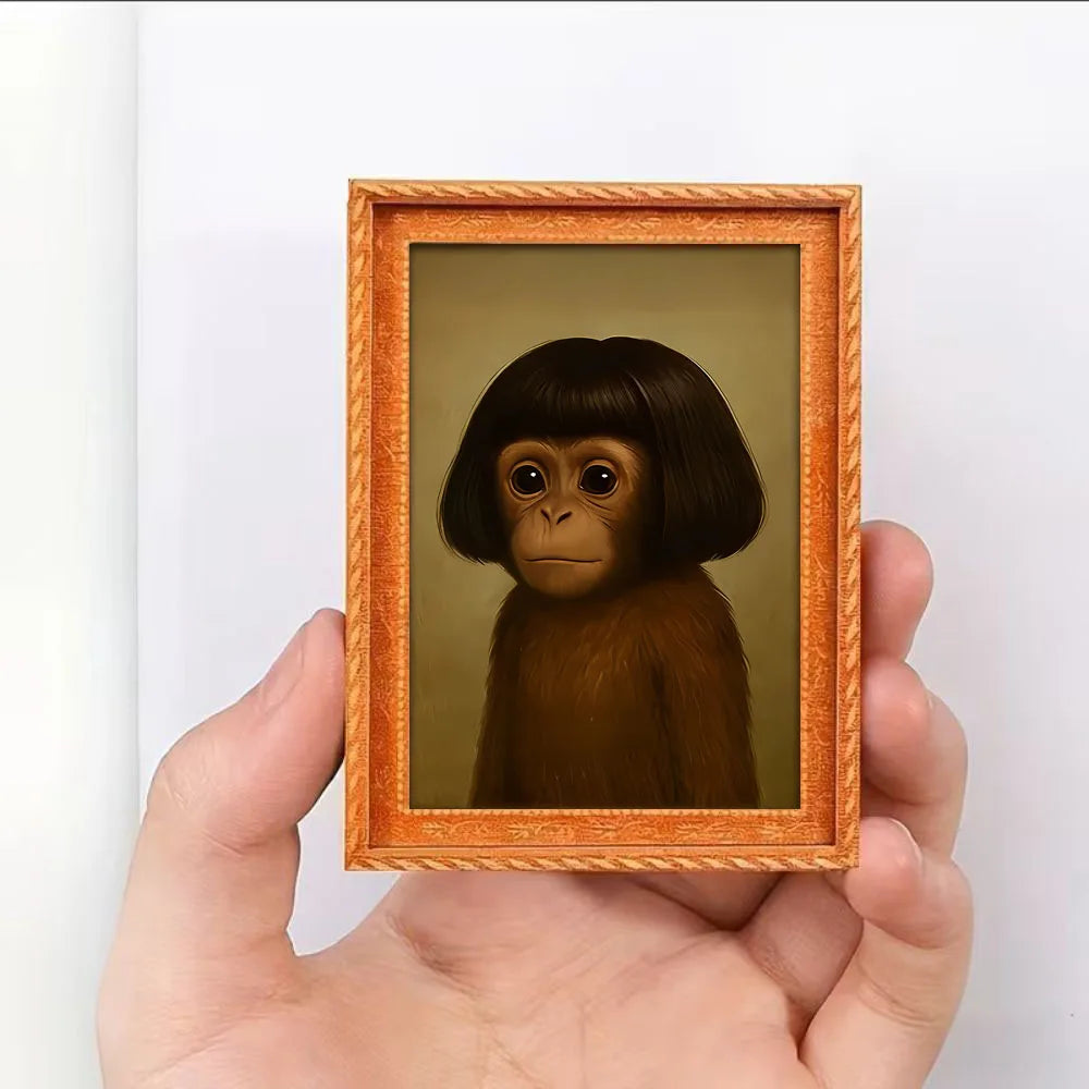 A hand holds a framed painting of a monkey's face in an orange wooden frame.