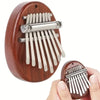 A wooden kalimba thumb piano with metal tines is shown being held by a hand.