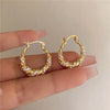 Gold twisted hoop earrings encrusted with small diamonds shown on a hand