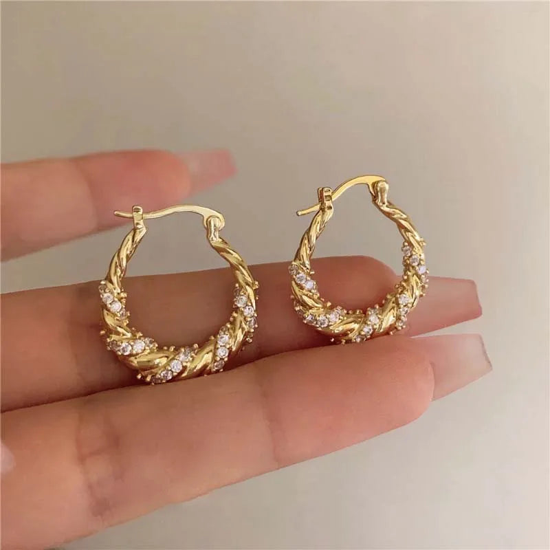 Gold twisted hoop earrings encrusted with small diamonds shown on a hand