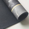 Roll of dark gray diatomite bath mat with a gold accent band lying next to a flat mat.