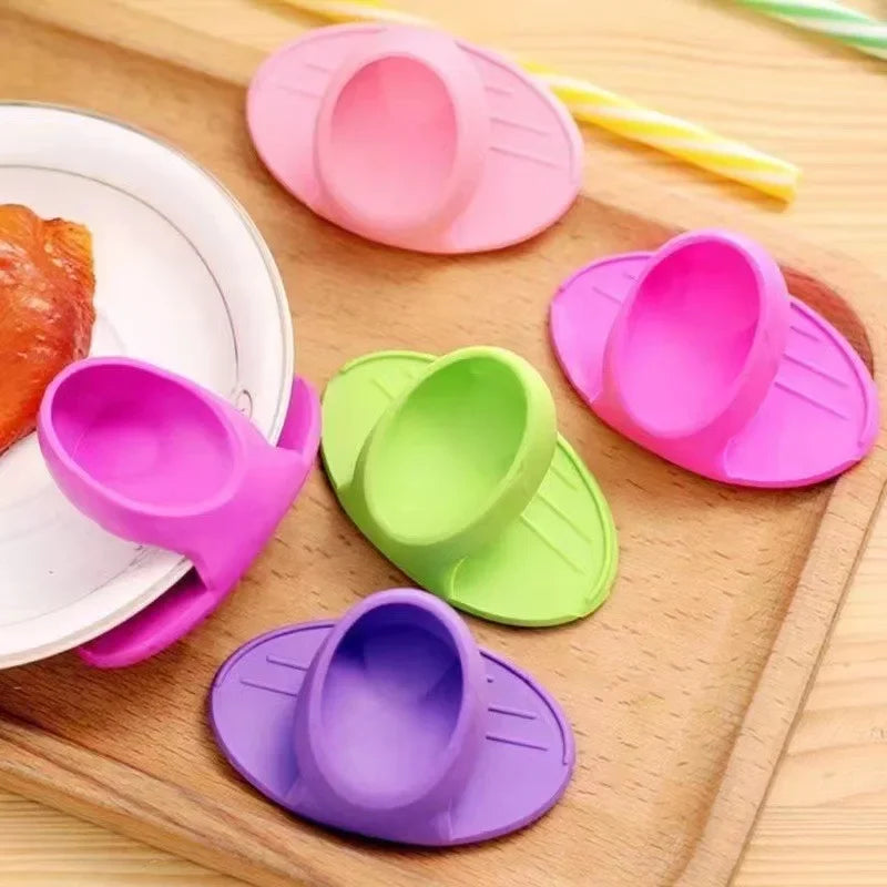 A collection of colorful heat-resistant silicone finger covers in pink, green, and purple resting on a wooden cutting board.