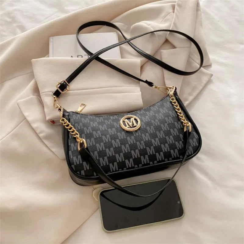 A black and gray patterned PU leather crossbody bag with gold chain accents resting on a white fabric background.