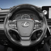 A close-up view of a black steering wheel with carbon fiber texture and controls in a car interior.