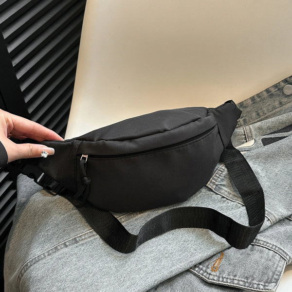 A black nylon crossbody waist bag is shown resting on a gray denim shirt.