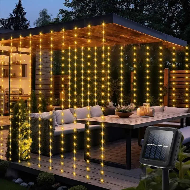Outdoor curtain lights illuminating a wooden deck and greenery at dusk