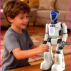 A young boy interacts with a white robot toy while building colorful blocks on a wooden table.