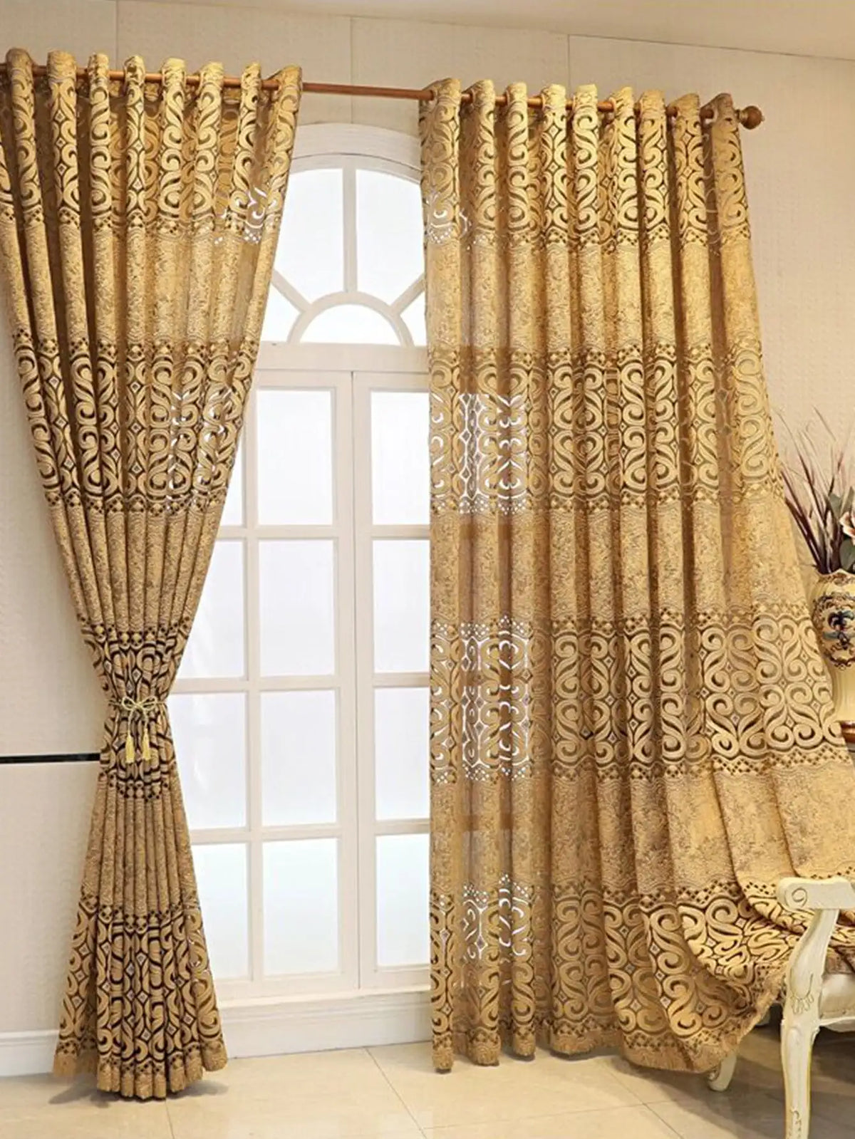 Cremefarbene und goldfarbene gemusterte Vorhänge hängen in einem weiß gerahmten Fenster.