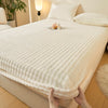 A white, textured fitted sheet with faux fur trim is being held by hands on a bed.