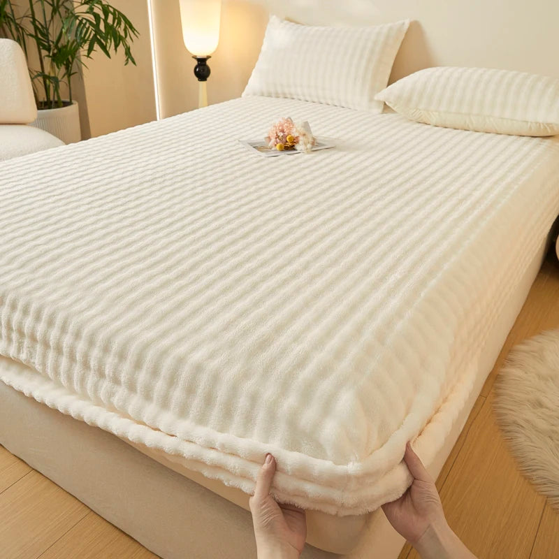 A white, textured fitted sheet with faux fur trim is being held by hands on a bed.