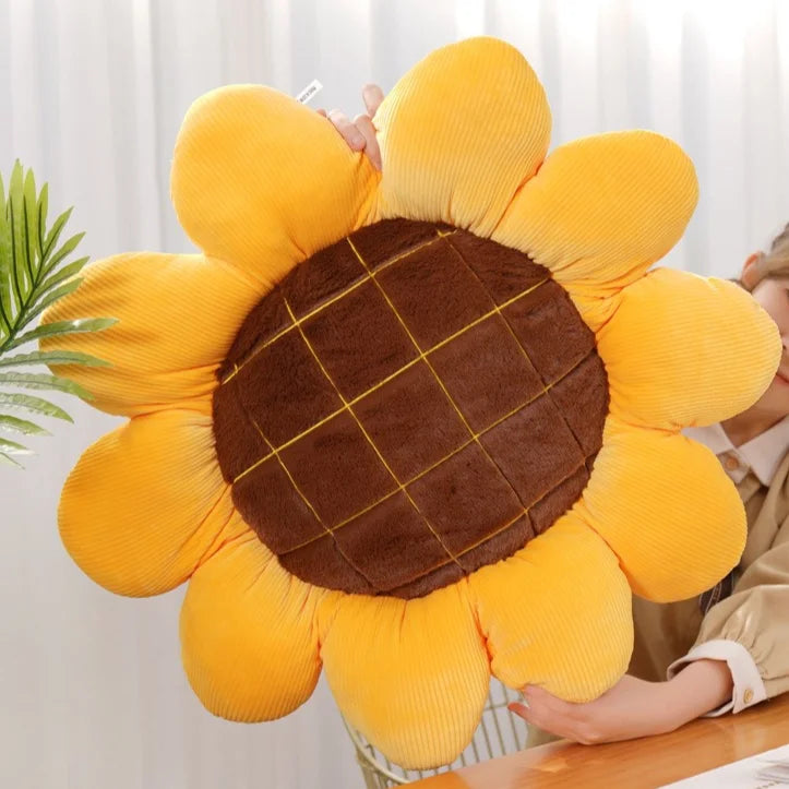 A yellow sunflower shaped floor pillow with a brown center is being held by a person.