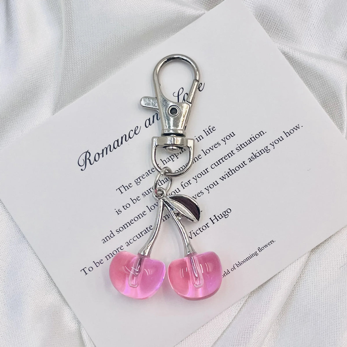 Un porte-clés cerise argenté et scintillant est présenté sur une carte blanche sur fond blanc.