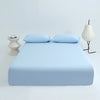 Light blue cooling ice-silk fitted sheet with two pillows and a modern lamp on a white background