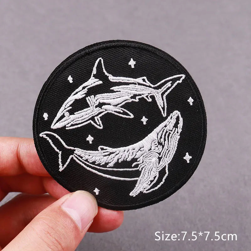 Black embroidered patch featuring a white silhouette of a shark and a whale on a gray background